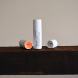 Two Vely tinted lip balm tubes on a wooden surface with a neutral background