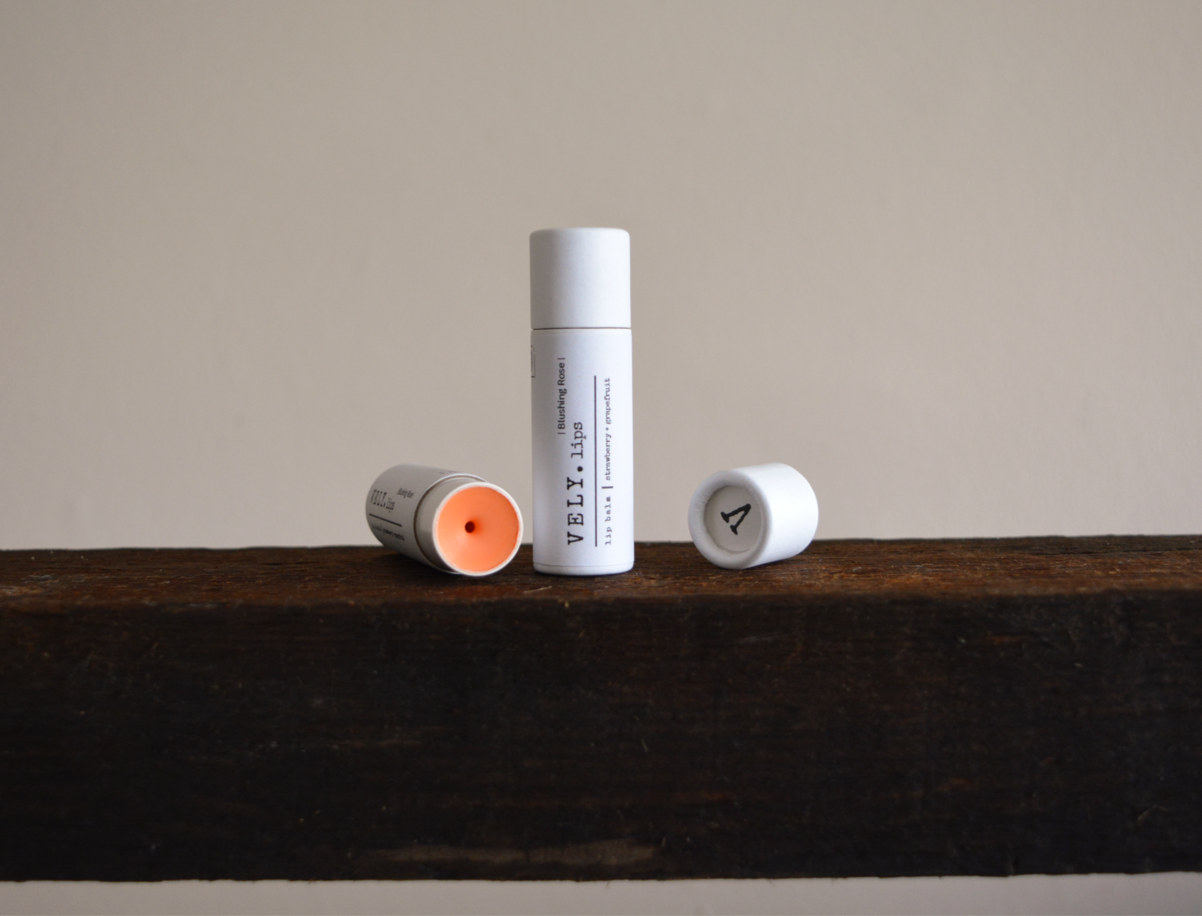 Two Vely tinted lip balm tubes on a wooden surface with a neutral background