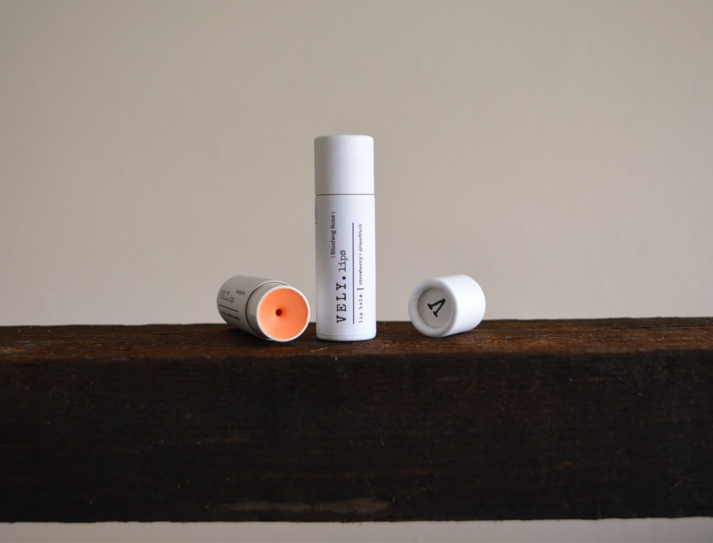 Two Vely tinted lip balm tubes on a wooden surface with a neutral background