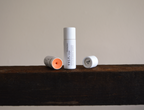 Two Vely tinted lip balm tubes on a wooden surface with a neutral background