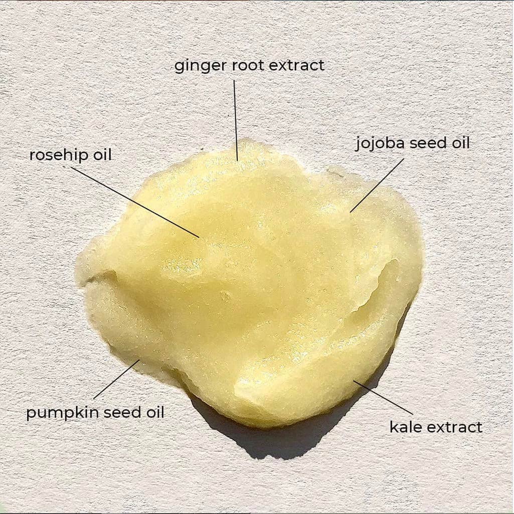Yellow coloured beauty balm with labeled ingredients on a textured grey background