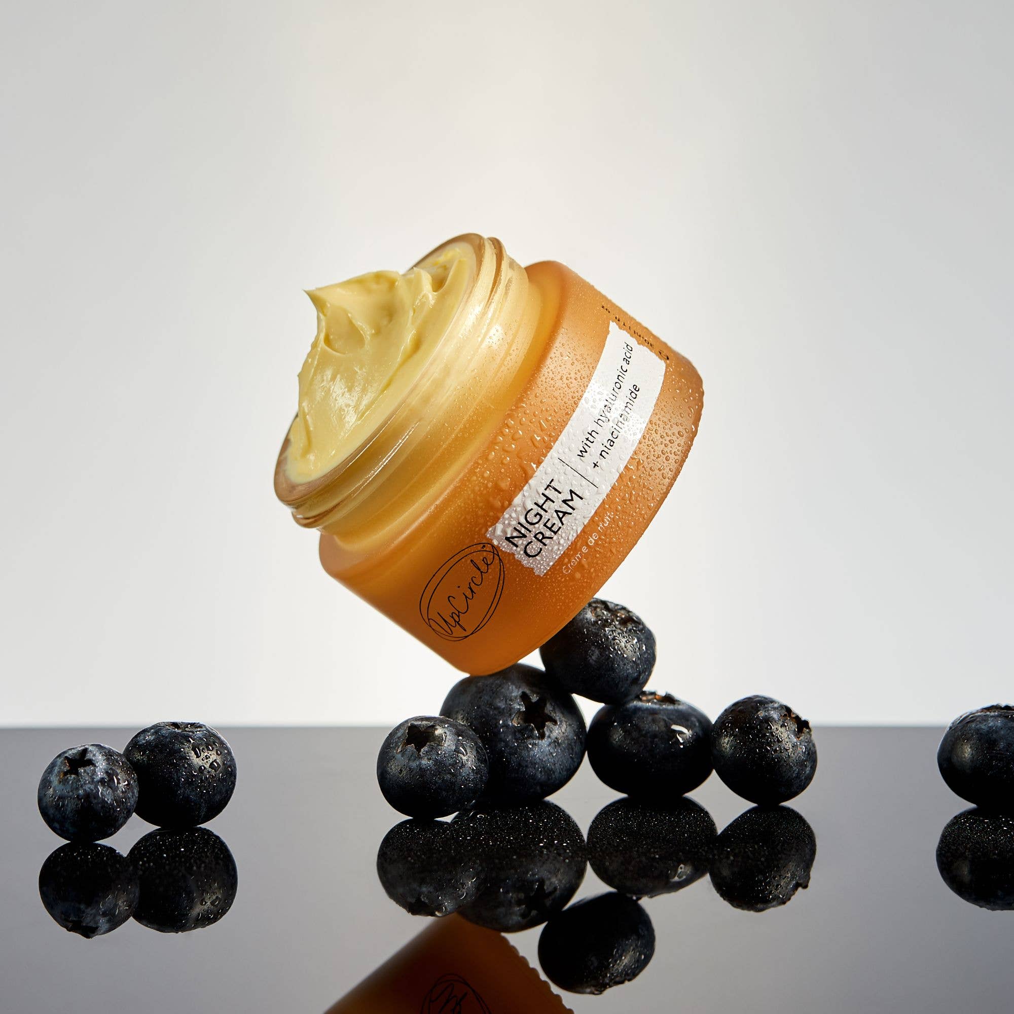 Jar of UpCircle Night Cream with blueberries on a reflective surface