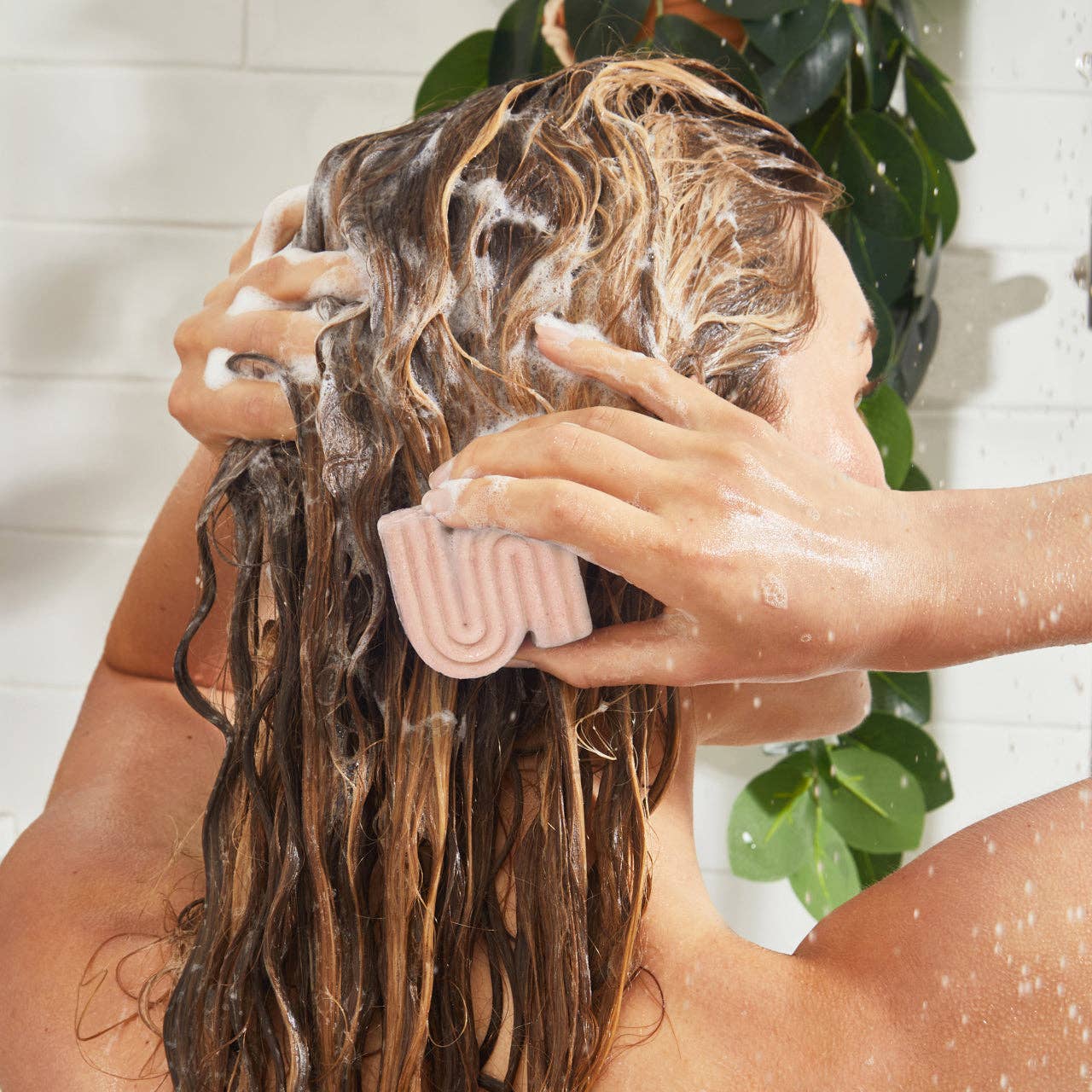 Person washing hair with a Kitsch shampoo bar in a bathroom setting