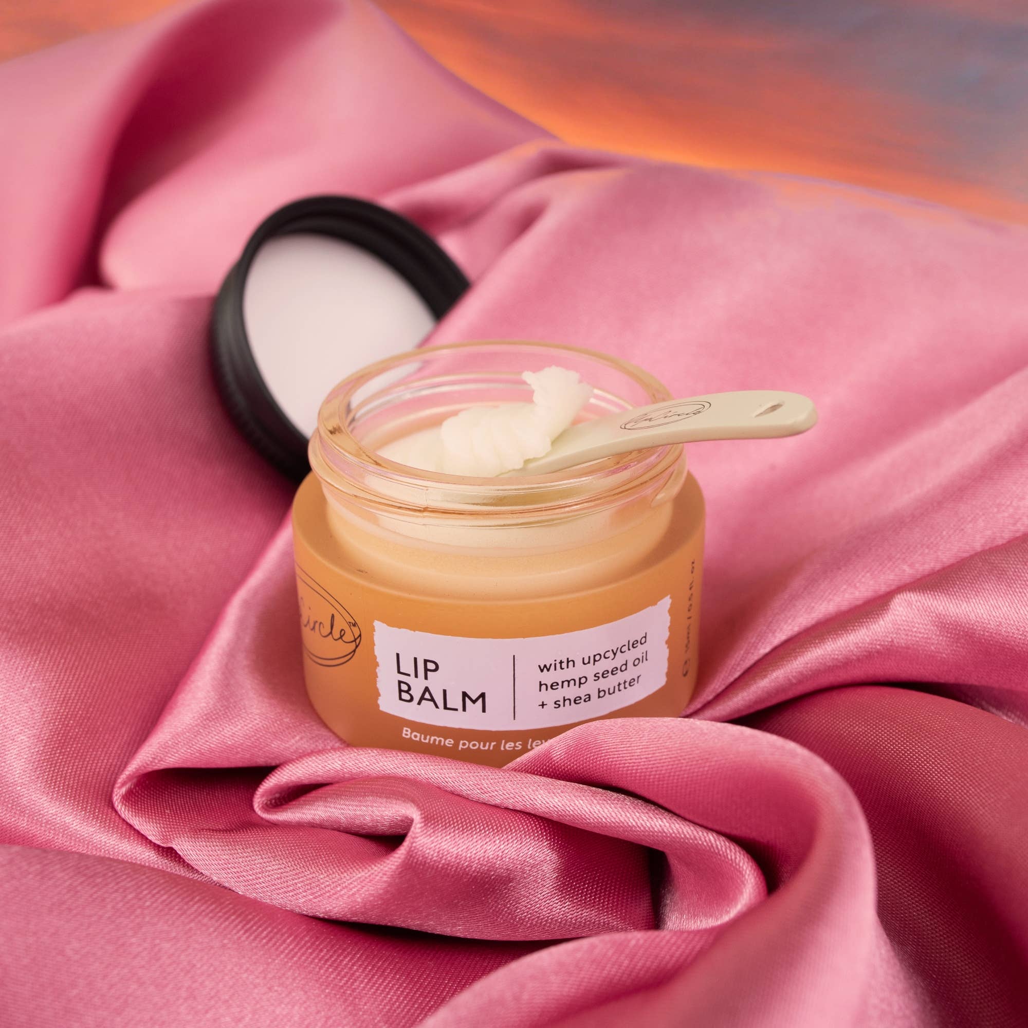 Jar of UpCircle lip balm with a spoon on pink fabric