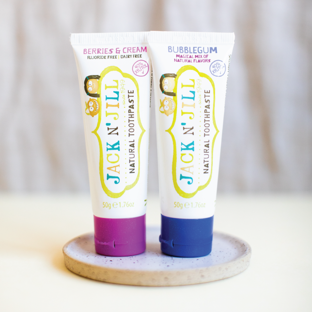 Two tubes of Jack N' Jill natural toothpaste on a wooden stand with a neutral background